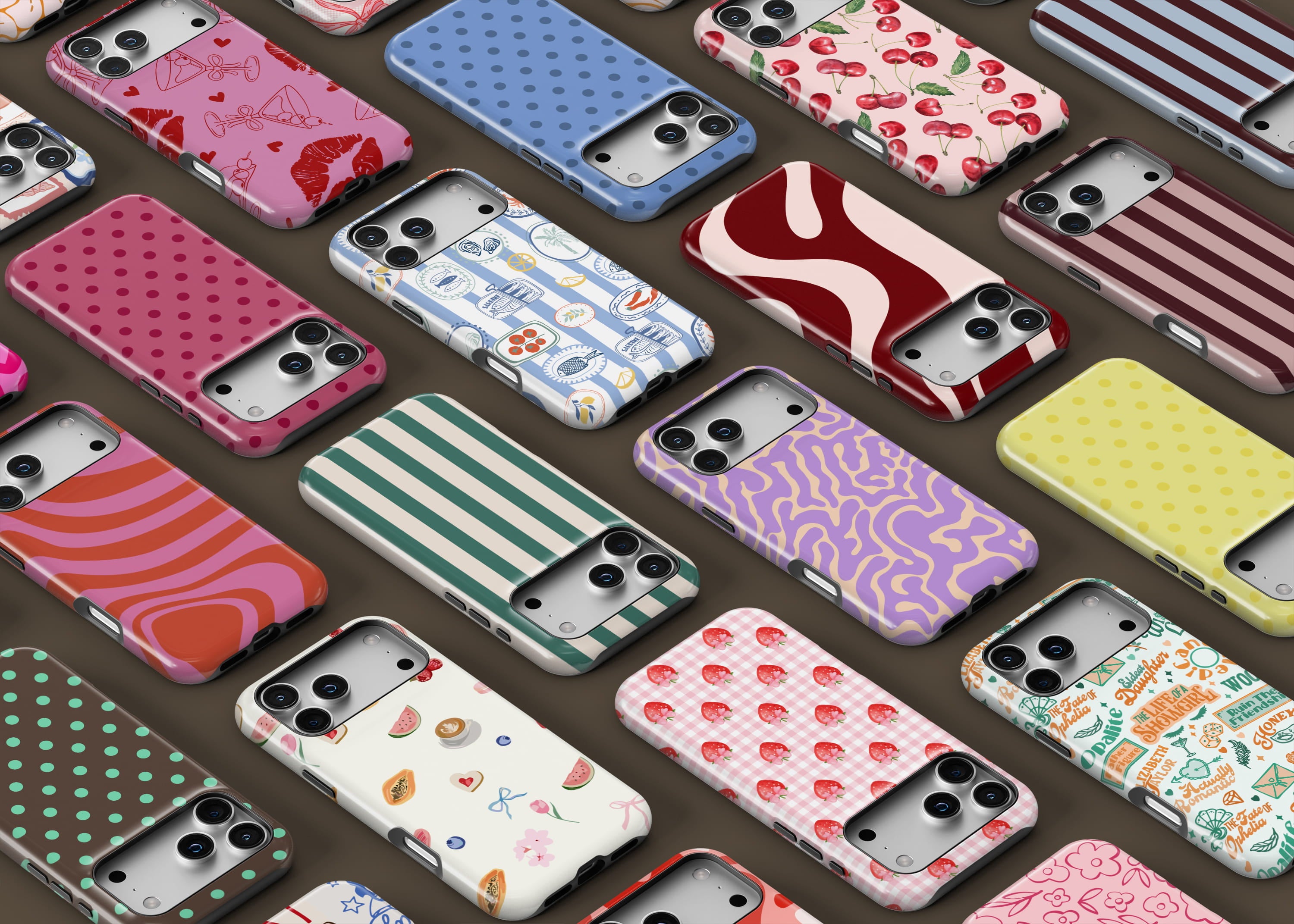 Flat lay of multiple patterned phone cases arranged diagonally on a brown background, featuring playful designs like polka dots, stripes, cherries, strawberries, abstract swirls, Mediterranean motifs, florals, and graphic prints in pink, red, blue, green, yellow, and purple tones.